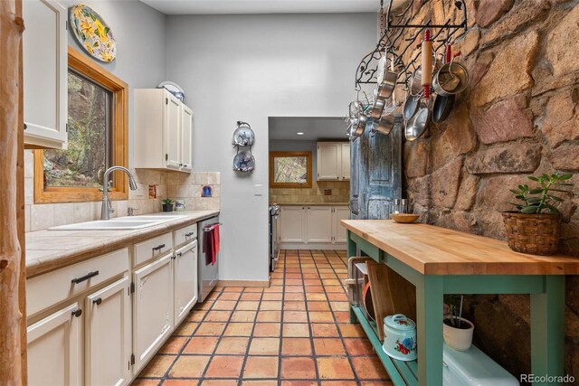 kitchen featuring a sink, stainless steel dishwasher, decorative backsplash, white cabinetry, and butcher block countertops