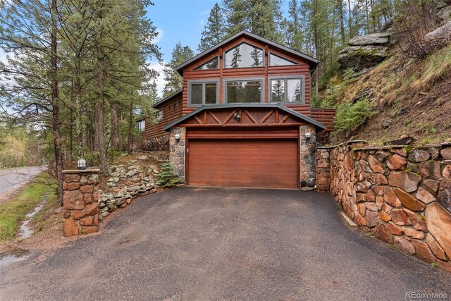 view of front of home featuring an attached garage, asphalt driveway, and stone siding