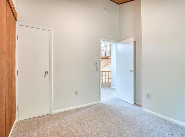 unfurnished bedroom with carpet floors, a high ceiling, and baseboards