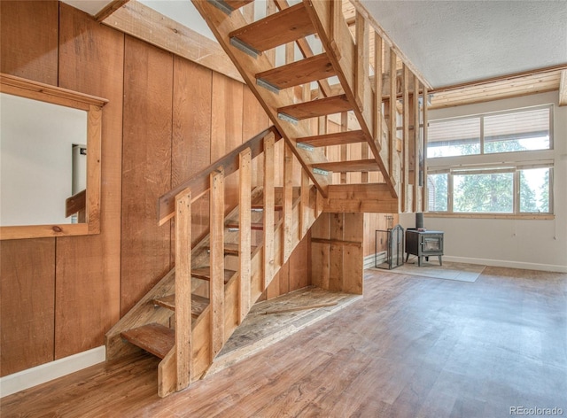 staircase with a wood stove, a textured ceiling, baseboards, and wood finished floors