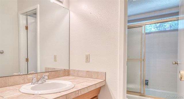 bathroom featuring combined bath / shower with glass door, a textured wall, and vanity