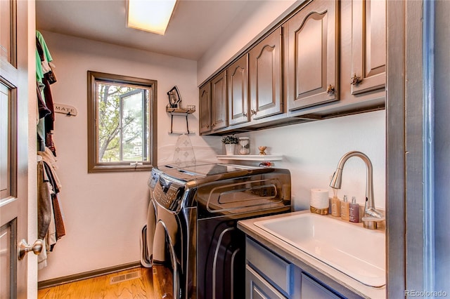 clothes washing area featuring sink, washing machine and dryer, cabinets, and light wood-type flooring