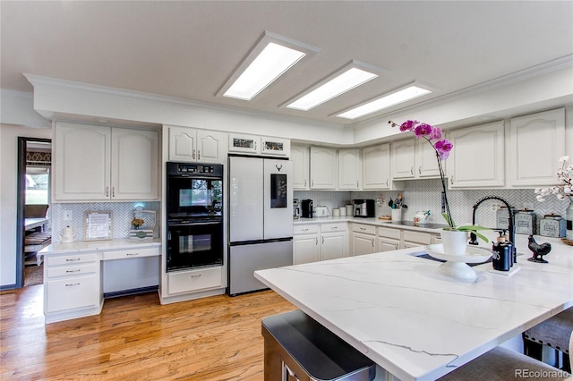 kitchen with white cabinetry, a kitchen breakfast bar, fridge, and black double oven