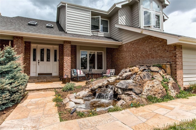 view of exterior entry featuring a garage, brick siding, and roof with shingles