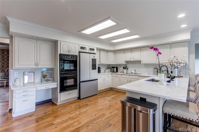 kitchen with light wood finished floors, a breakfast bar, a peninsula, black appliances, and a sink