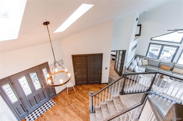 foyer with a skylight, a notable chandelier, high vaulted ceiling, light wood-type flooring, and stairs