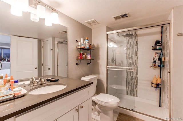 bathroom with toilet, vanity, a shower stall, and visible vents