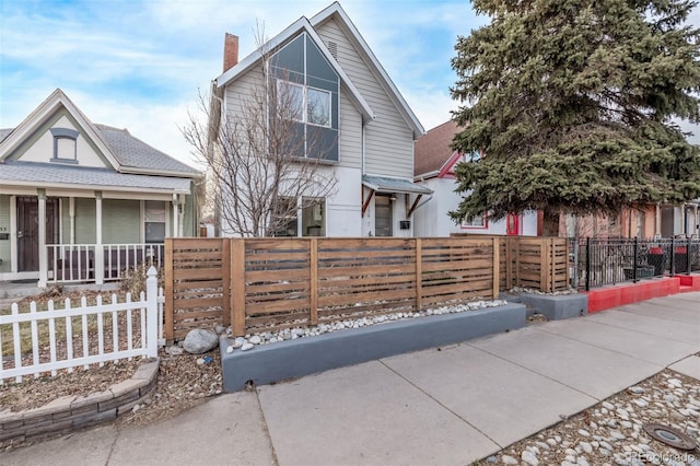 view of front of property with a porch, a chimney, and a fenced front yard