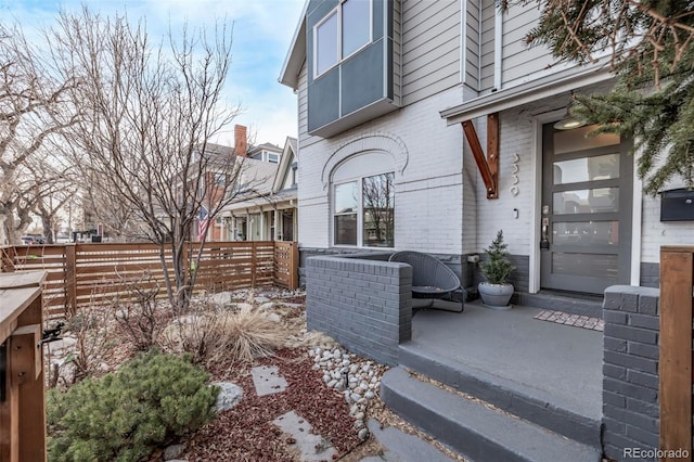 view of exterior entry with fence and brick siding