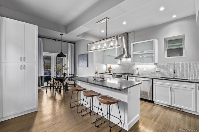 kitchen with dark countertops, wall chimney exhaust hood, a breakfast bar, stainless steel appliances, and a sink