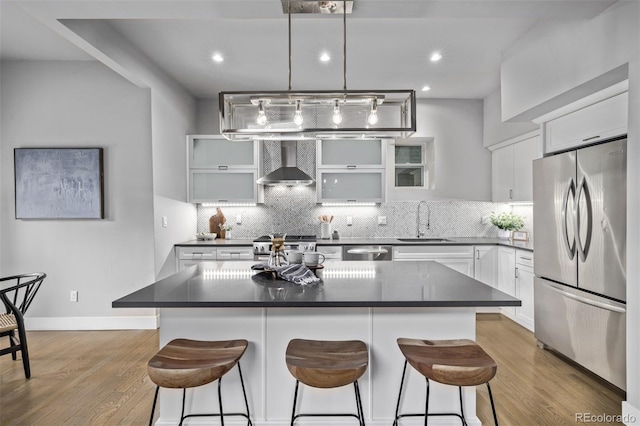 kitchen featuring stainless steel appliances, dark countertops, backsplash, a sink, and wall chimney exhaust hood