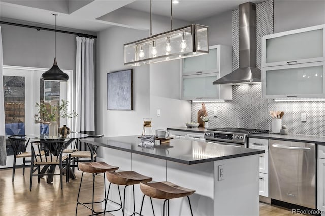 kitchen featuring dark countertops, wall chimney exhaust hood, a center island, stainless steel appliances, and backsplash