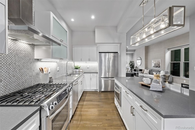 kitchen with decorative backsplash, appliances with stainless steel finishes, dark wood-type flooring, white cabinets, and wall chimney range hood