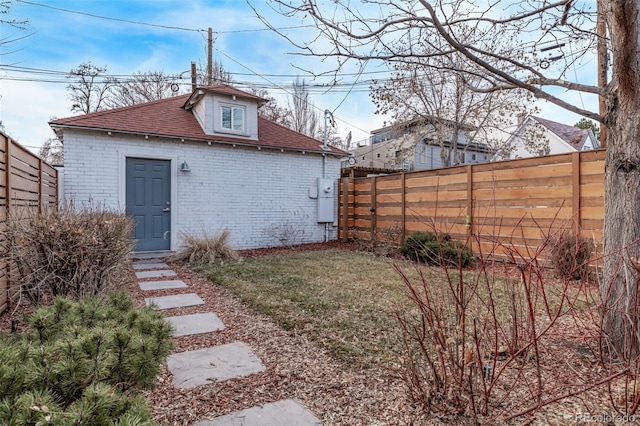 rear view of property featuring an outbuilding, brick siding, roof with shingles, and fence