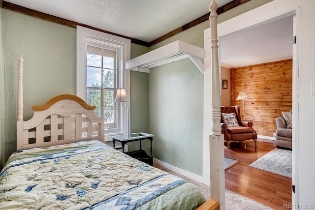 bedroom with ornamental molding, wooden walls, and light hardwood / wood-style flooring