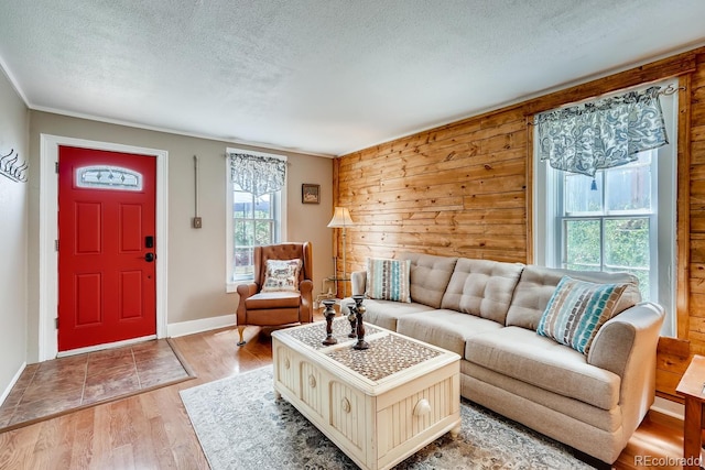 living room with wooden walls, light hardwood / wood-style floors, a textured ceiling, and ornamental molding