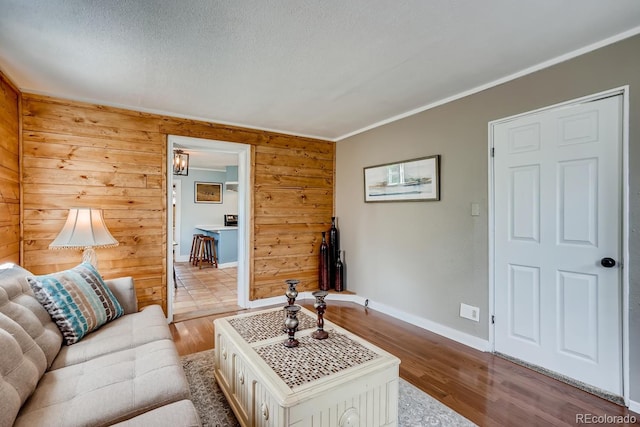 living room featuring a textured ceiling, light wood-type flooring, ornamental molding, and wooden walls