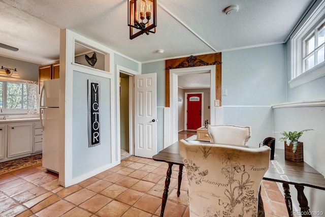 interior space featuring a kitchen breakfast bar, white fridge, a textured ceiling, white cabinets, and ornamental molding