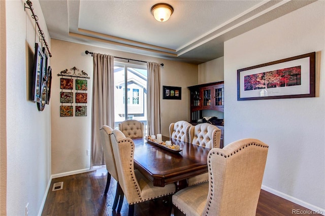 dining space featuring visible vents, a raised ceiling, dark wood-type flooring, and baseboards