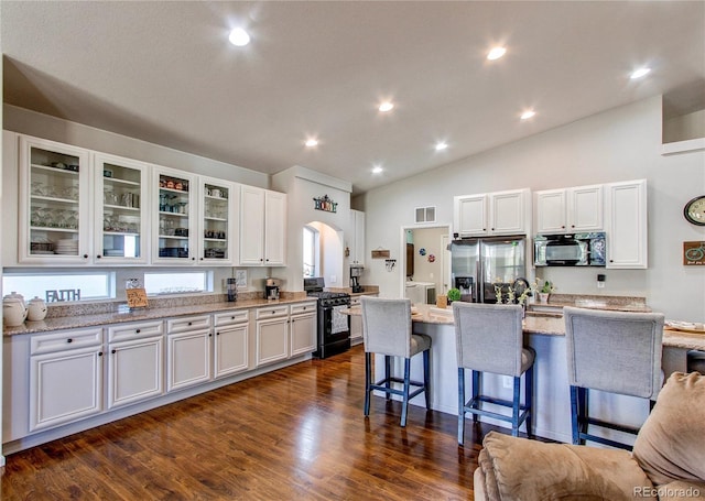 kitchen featuring a breakfast bar area, dark wood-style floors, black appliances, glass insert cabinets, and white cabinetry