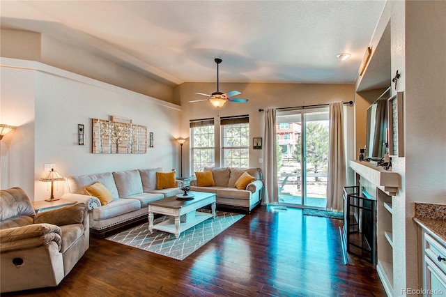 living area with vaulted ceiling, a fireplace, a ceiling fan, and wood finished floors