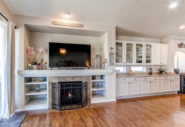 unfurnished living room featuring arched walkways, recessed lighting, a fireplace, and wood finished floors