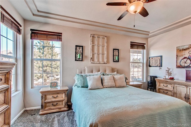 carpeted bedroom featuring ceiling fan, a raised ceiling, and baseboards