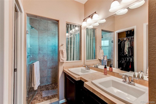 full bathroom with a sink, a walk in closet, double vanity, and a tile shower