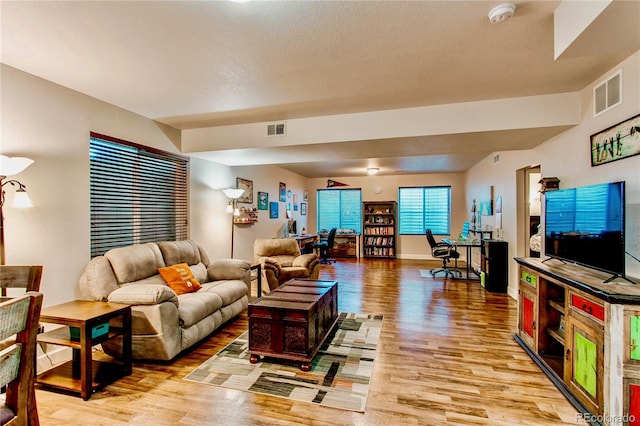 living room featuring visible vents, baseboards, a textured ceiling, and light wood-style flooring