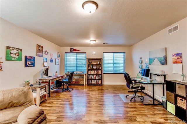 office with baseboards, visible vents, a textured ceiling, and light wood-style floors