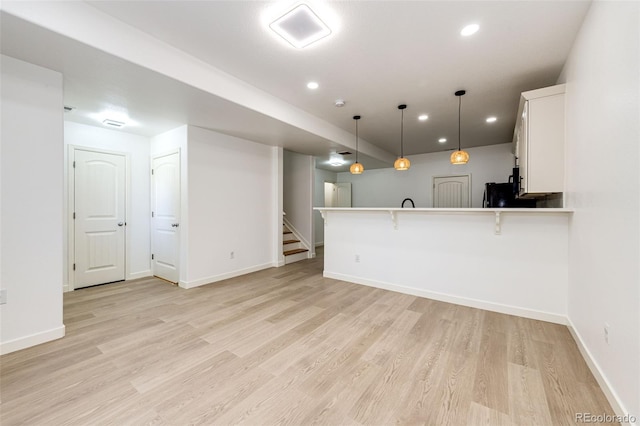 kitchen featuring kitchen peninsula, light wood-type flooring, white cabinetry, hanging light fixtures, and a breakfast bar area