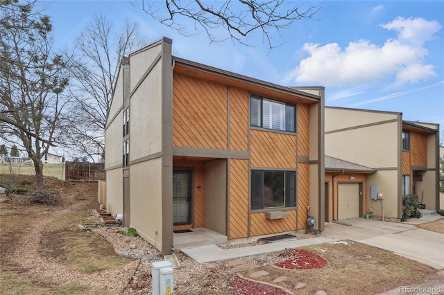 view of front facade featuring stucco siding, concrete driveway, and fence