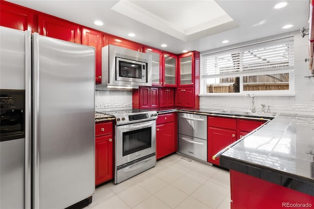 kitchen featuring red cabinetry, a warming drawer, a sink, tasteful backsplash, and appliances with stainless steel finishes