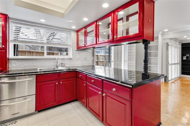 kitchen featuring tasteful backsplash, red cabinets, dark countertops, and a sink