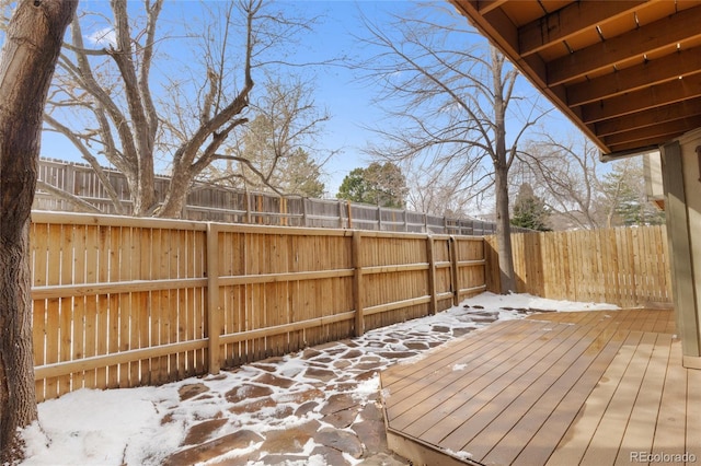 snow covered deck with a fenced backyard