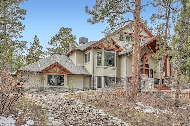 view of front of house featuring stone siding, roof with shingles, and stucco siding