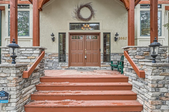 doorway to property with stone siding, stucco siding, and a porch