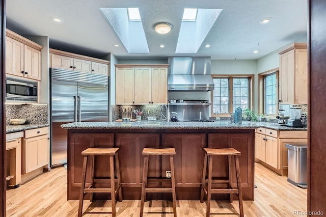 kitchen featuring built in appliances, a breakfast bar area, a skylight, and wall chimney exhaust hood