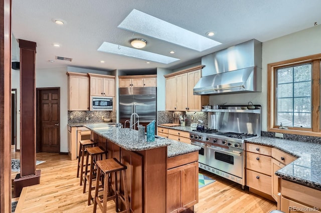 kitchen with visible vents, built in appliances, a skylight, wall chimney exhaust hood, and a sink