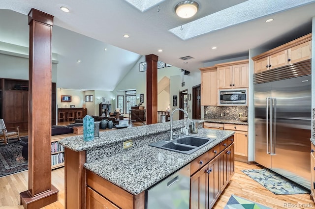 kitchen featuring a center island with sink, ornate columns, visible vents, a sink, and built in appliances