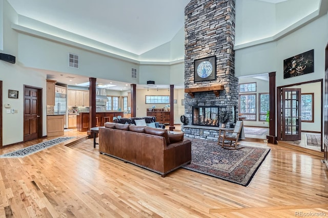 living room with light wood-style flooring, a fireplace, visible vents, and ornate columns