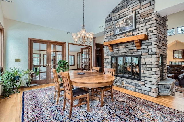 dining space featuring a notable chandelier, french doors, a stone fireplace, and wood finished floors