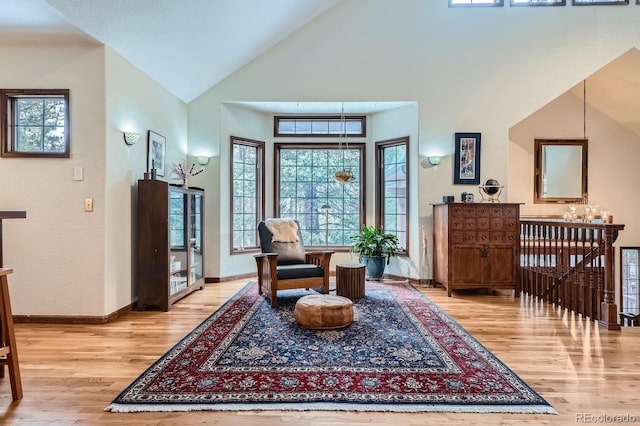 living area with baseboards, high vaulted ceiling, light wood-style floors, a notable chandelier, and an upstairs landing