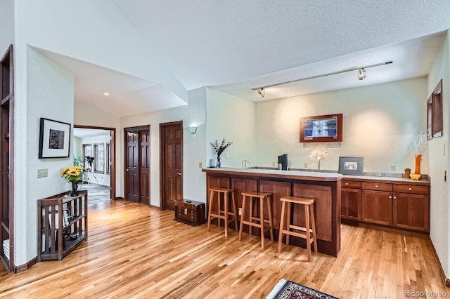 kitchen featuring brown cabinets, a textured ceiling, a breakfast bar area, light wood finished floors, and lofted ceiling