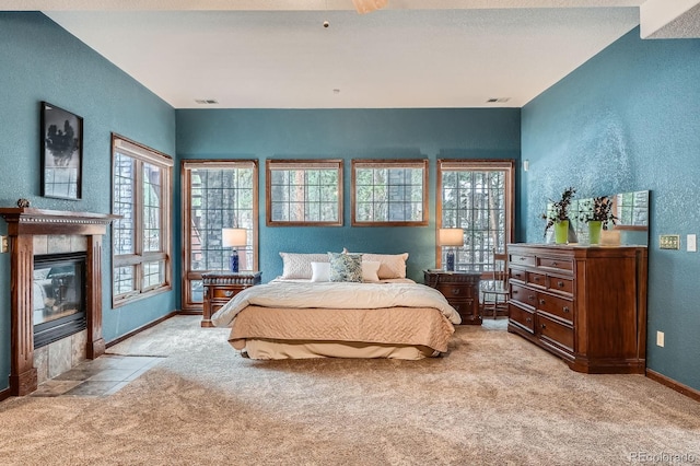 carpeted bedroom featuring visible vents, multiple windows, a fireplace, and a textured wall