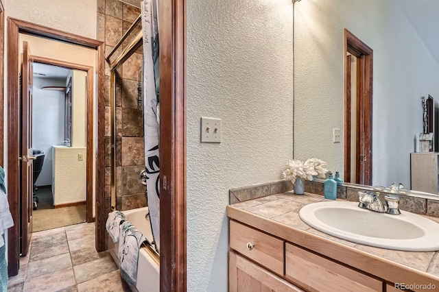 full bathroom featuring washtub / shower combination, vanity, and a textured wall