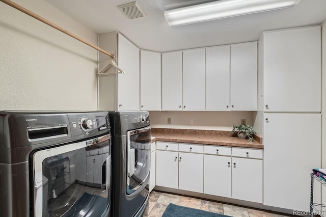 laundry area with washing machine and clothes dryer, visible vents, cabinet space, and stone finish floor