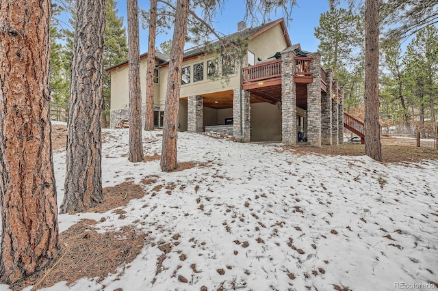 snow covered property with stairs, a wooden deck, stone siding, and stucco siding