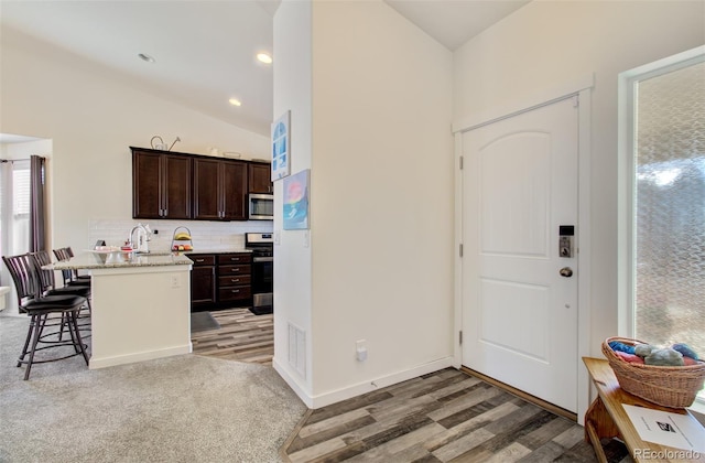 2734 Grand Prix Ct, Colorado Springs, CO 80922 - kitchen with stainless steel appliances, a breakfast bar area, dark brown cabinetry, vaulted ceiling, and tasteful backsplash