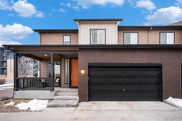 view of front of house with an attached garage, covered porch, brick siding, driveway, and board and batten siding